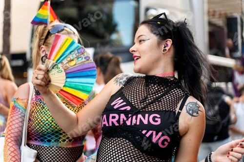 Preview: Young women celebrating at gay pride parade with rainbow fan