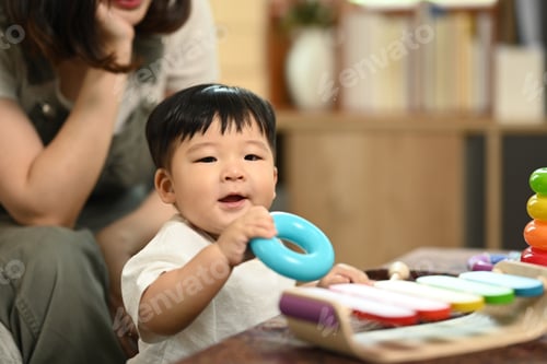 Preview: Cute baby boy sitting on the floor, playing with colorful toys with mother.