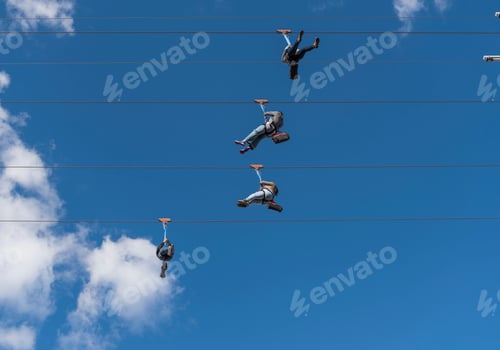 Preview: Thrillseekers ziplining against a clear blue sky.