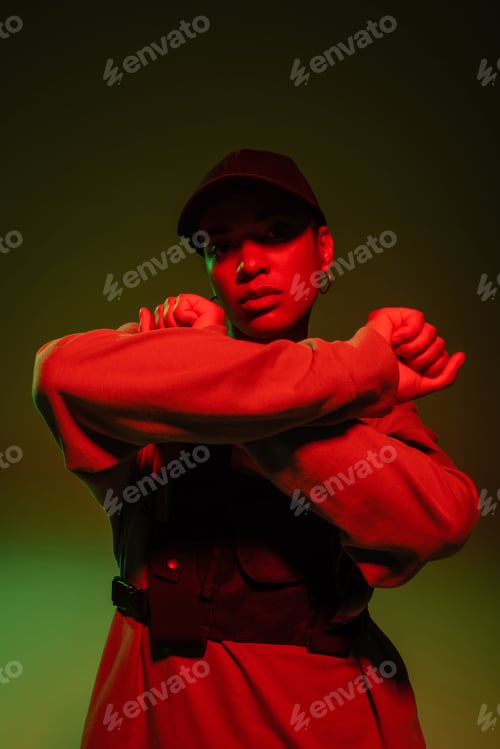 Preview: african american woman in sweatshirt and baseball cap posing with crossed arms on green with red
