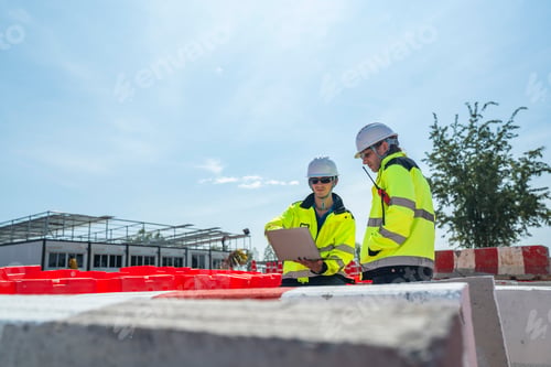 Preview: Two engineers sit amidst red-and white barricades at a construction site.