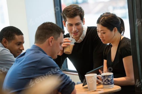 Preview: A group of people sitting at a table in a coffee shop. Looking at the screen of a digital tablet.