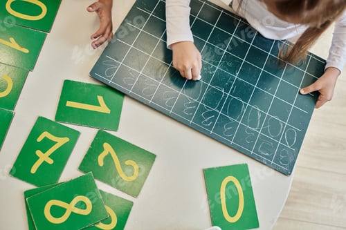 Preview: top view of girl writing number zero on chalkboard, learning how to count in Montessori school