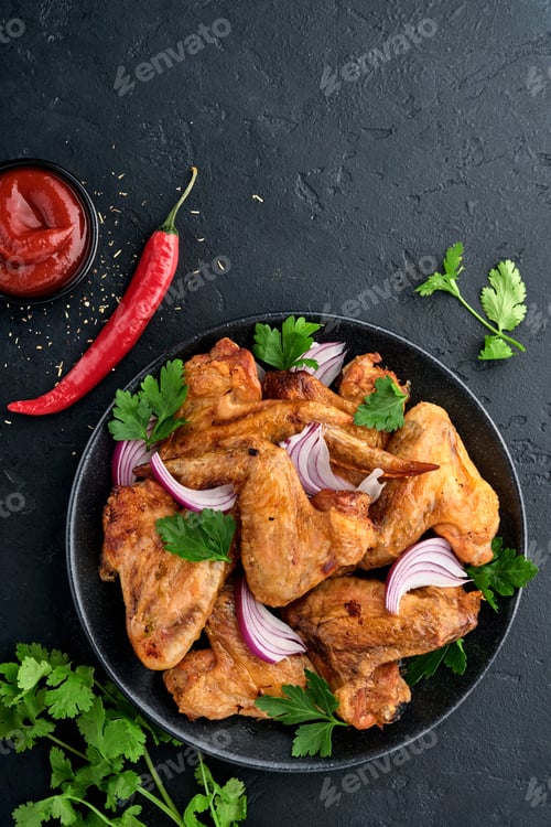 Preview: Grilled chicken wings or roasted bbq with spices and tomato salsa sauce on a black plate. Top view w