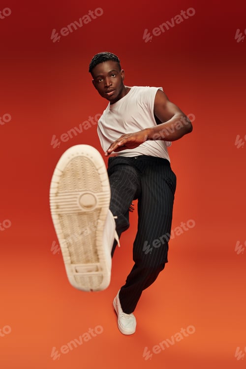 Preview: stylish african american man in daring pose with outstretched leg on red and orange backdrop