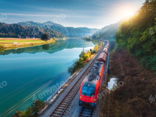 Preview: Aerial view of red train moving near river in alpine mountains