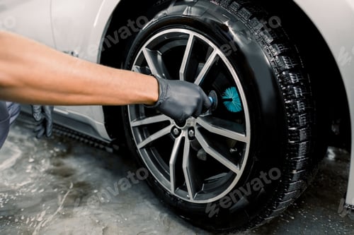 Preview: Auto wash service. Cropped close up image of male hands in black protective gloves, cleaning alloy