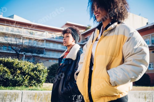 Preview: Two cool young female friends on urban sidewalk, side view