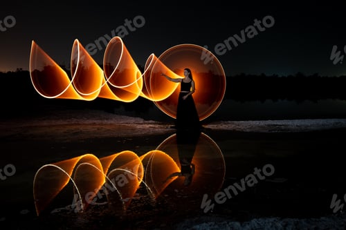 Preview: Woman posing for light painting with bright lights in the dark. Reflection in the water