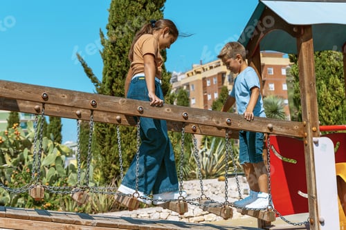 Preview: Kid girl and boy playing on playground in park in a warm sunny day