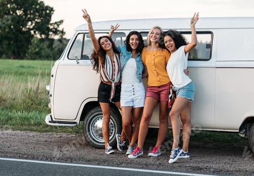 Preview: Four smiling women standing together on the roadside near a car during vacation