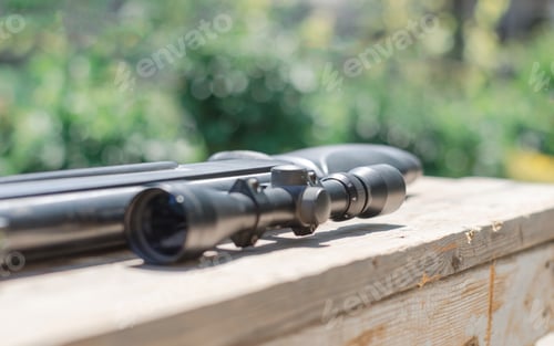 Preview: Sniper rifle lies on a wooden background. Optical sight close-up.