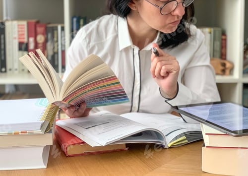 Preview: Back to school: young millennial female student is studying from home. Pile of books and tablet