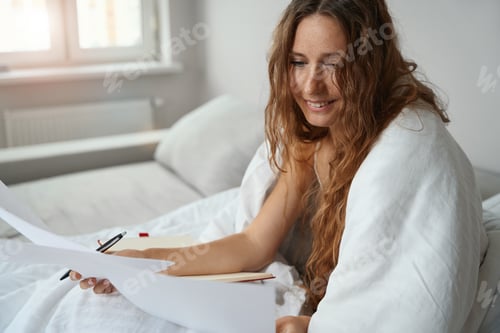 Preview: Woman studying text document in bed covered with a blanket