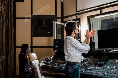 Preview: attractive sound producer applauding in recording studio near mixing console