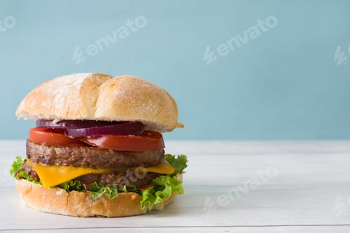 Preview: Delicious double burger with lettuce, tomato, onion, and cheese filling a white bun on a table