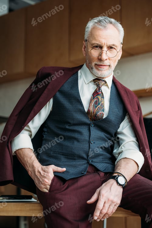 Preview: handsome mature man with jacket on shoulders sitting on table
