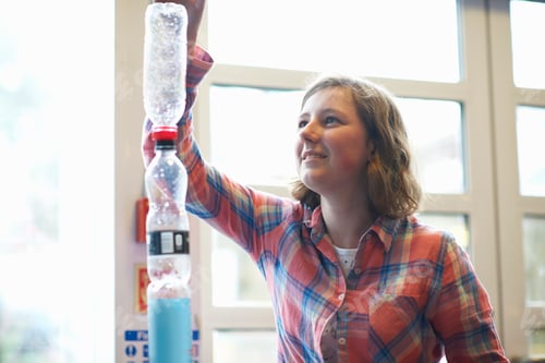 Preview: Teenage female student stacking plastic bottles for experiment in college classroom