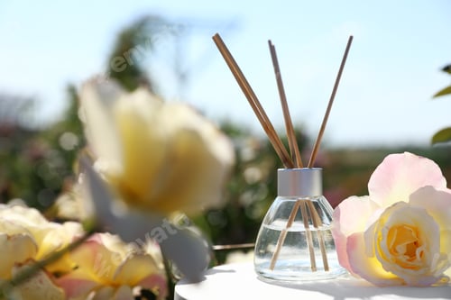 Preview: Reed air freshener with oil and fresh rose on table against blurred background. Space for text