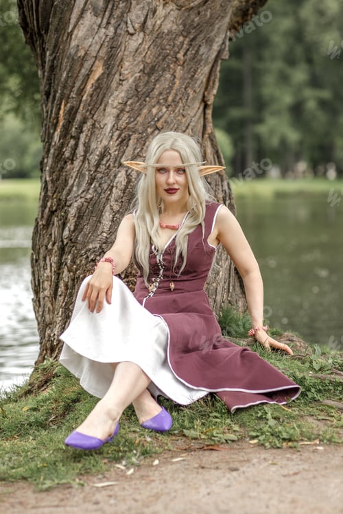 Preview: Young elf girl with blond long hair. Medieval elven princess in a burgundy dress in the forest