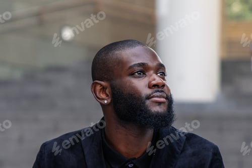 Preview: closeup of a Thoughtful and relaxed African businessman sitting outside office in financial district