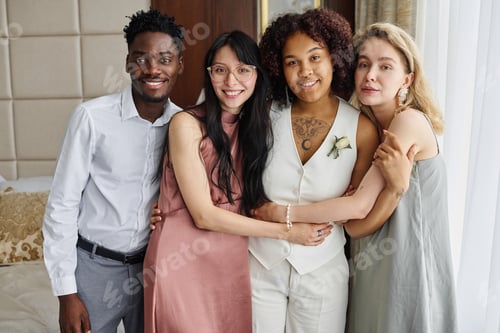Preview: Happy young intercultural women and guy standing by African American bride
