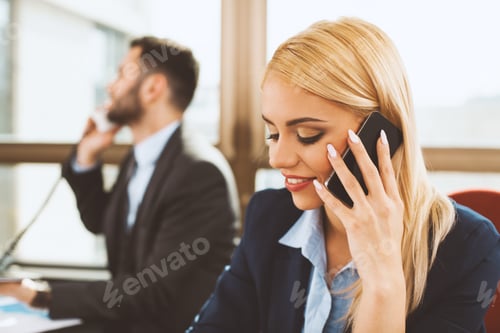 Preview: Young businesswoman talking on the phone with business man in the background in the office