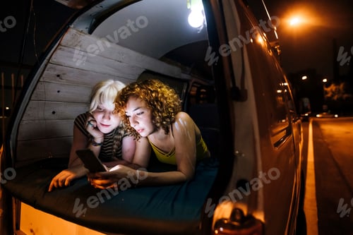 Preview: Two friends sharing a moment with a smartphone in a cozy van at night