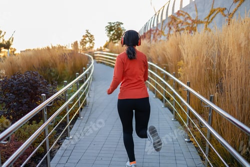 Preview: young beautiful and happy Asian Korean woman in sportswear listening to music with headphones runnin