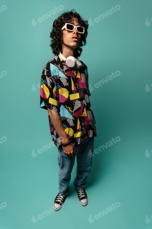 Preview: Syncopated young Latin American male with curly hair sunglasses looking at camera while standing