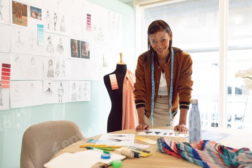 Preview: Beautiful mixed race female fashion designer looking at camera while working on table