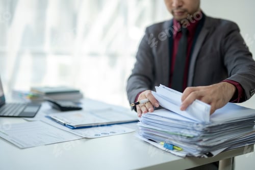 Preview: A man is sitting at a desk with a pile of papers in front of him