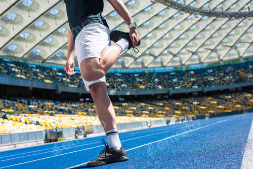 Preview: cropped shot of man stretching on running track at sports stadium