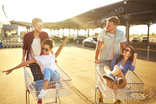 Preview: Group of happy young people having fun on shopping trolleys. Young people racing on shopping cart.