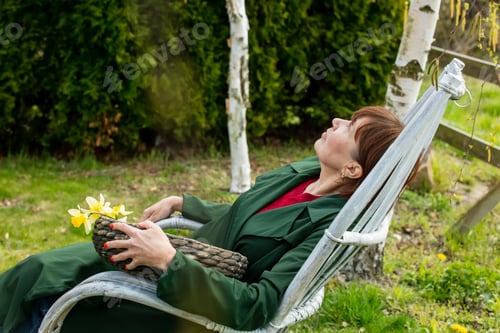 Preview: Senior woman sits in armchair in spring time garden