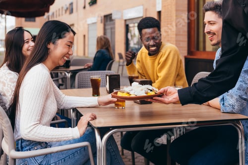 Preview: interracial gathering of friends happy because a waiter is serving them food