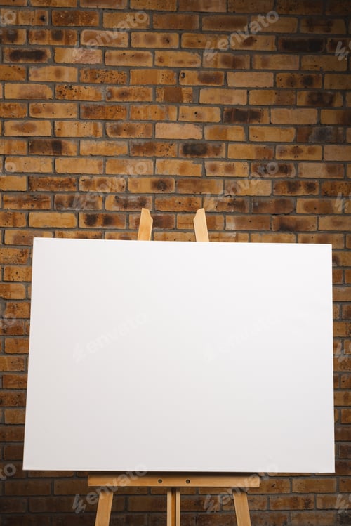 Preview: White canvas on wooden easel and copy space on brick wall background