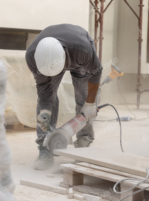 Preview: Craftsman in grey work clothes and helmet cutting marble piece during construction