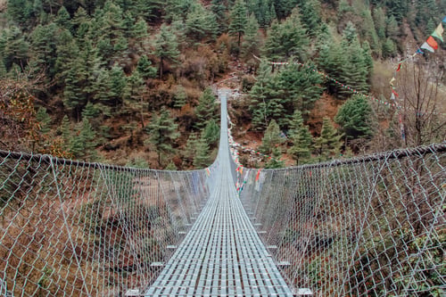 Preview: Trekker crossing metal suspension bridge in Nepal, Himalayas