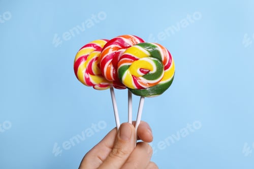 Preview: Woman holding bright tasty lollipops on light blue background, closeup