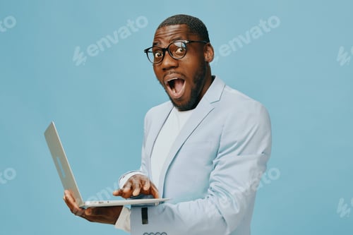Preview: African man in trendy attire using laptop, excited expression, light blue background, modern fashion