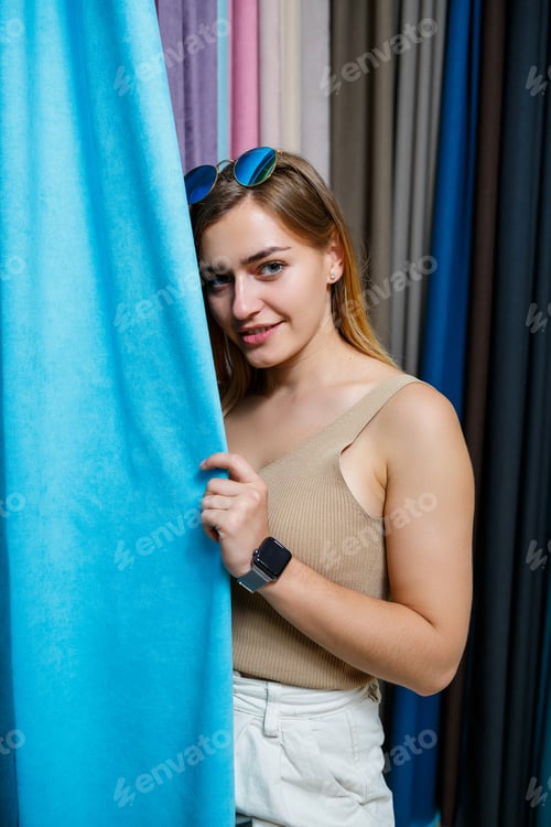 Preview: Young woman choosing fabric for new curtains in a store. Samples of the curtain hang on hangers