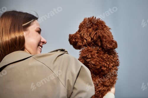 Preview: A young pretty blonde girl hugs her pet red toy poodle and smiles. The dog sits in the arms of the