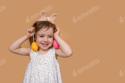 Preview: Close-up Emotional Positive portrait of little girl with bunny ears on head, plays with eggs