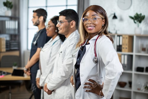 Preview: Confident female afro-american doctor in front of team, looking at camera and smiling