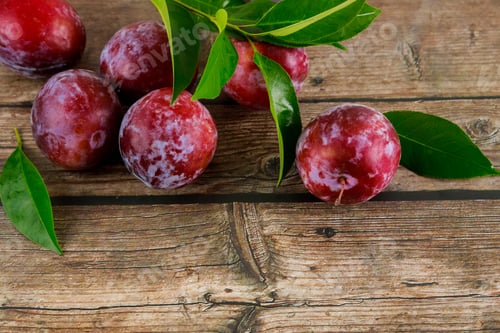 Preview: Red plum with green leaves on wooden background.