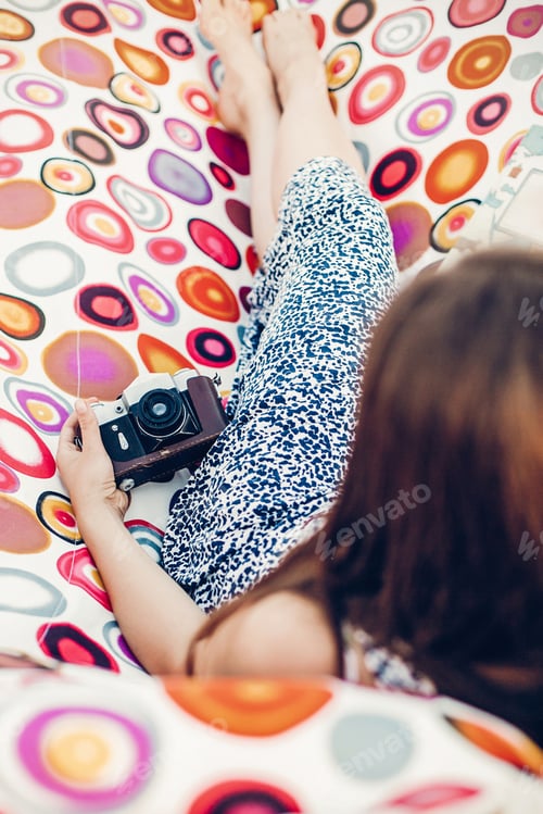 Preview: Romantic brunette girl in beautiful dress lying on a hammock with film camera