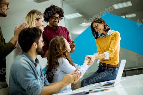 Preview: Group of young coworkers interacting around a table and handshaking in the office