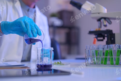 Preview: Cropped shot scientist pours a purple liquid into a beaker during laboratory testing