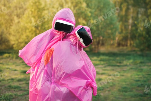 Preview: Closeup shot of two people in pink plastic raincoats and VR headset kissing each other
